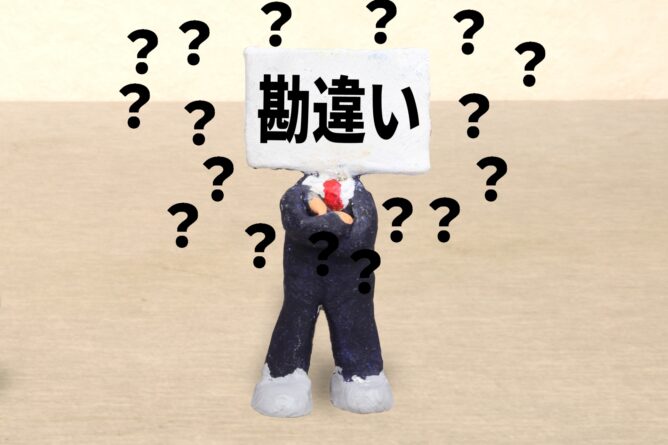 Clay figurine holding a sign with the Japanese word 勘違い (misunderstanding) surrounded by large question marks, conveying confusion or a mistaken assumption.