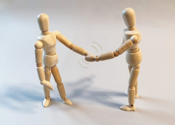 22111514_m | M Virtual(エムバーチャル) - Vライバーマネジメント事務所 Two wooden mannequin figures shake hands in a friendly greeting gesture.