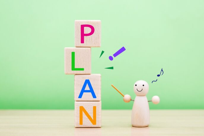24464537_m | M Virtual(エムバーチャル) - Vライバーマネジメント事務所 Wooden blocks stacked to spell PLAN (P on top, L, A, N below) with a small wooden figure pointing at them, set against a light green background—conveys planning or teaching.