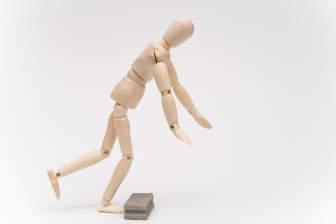 25323265_m 1 | M Virtual(エムバーチャル) - Vライバーマネジメント事務所 Wooden mannequin stepping onto a small gray brick, against a white background, as if overcoming an obstacle.