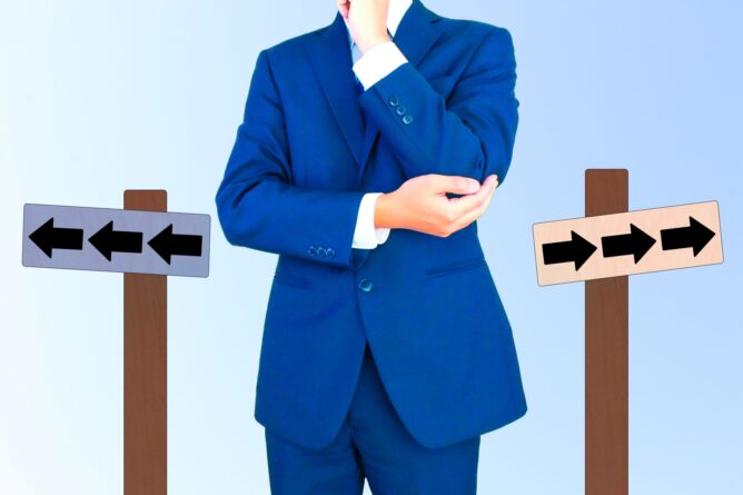 Person in a blue suit stands at a crossroads, with signs pointing left and right, contemplating which direction to take.