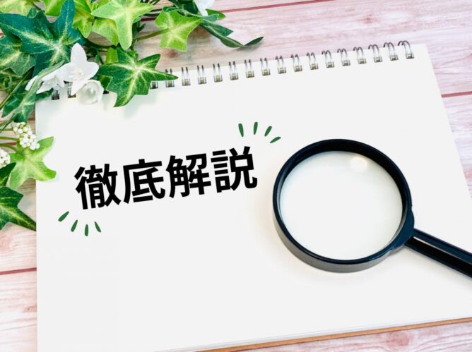Notebook page with bold Japanese text 徹底解説, a magnifying glass resting on the corner, and green ivy decorations on a wooden desk top.