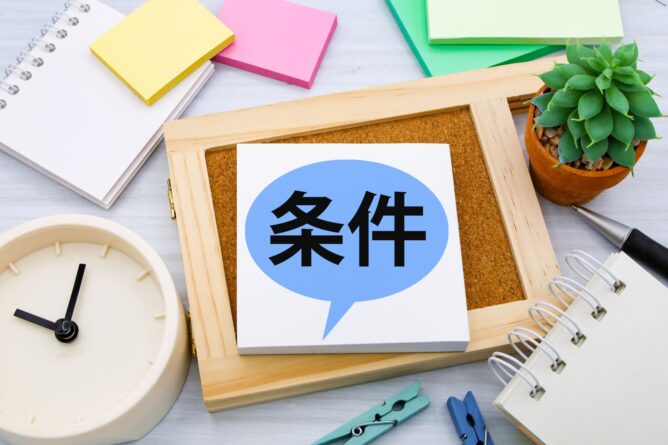 Sticky note on a corkboard with a blue speech bubble showing the Chinese word 条件 (conditions) on an office desk, with clock and plants nearby.