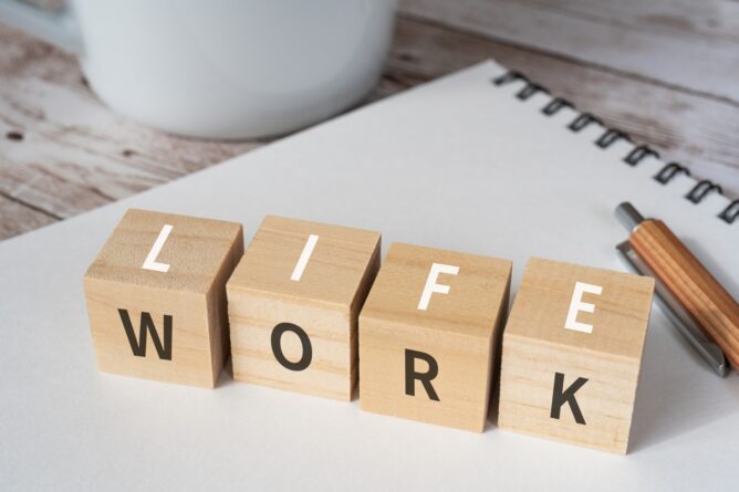 Wooden letter blocks spell the word WORK on a desk beside a notebook and pencil.
