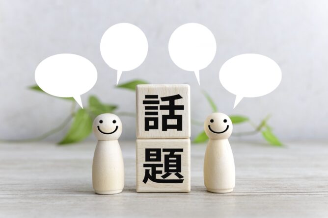 33118882_m | M Virtual(エムバーチャル) - Vライバーマネジメント事務所 Three wooden figures with speech bubbles surround a block tower that reads 話題, symbolizing a discussion about topics (topic talk).