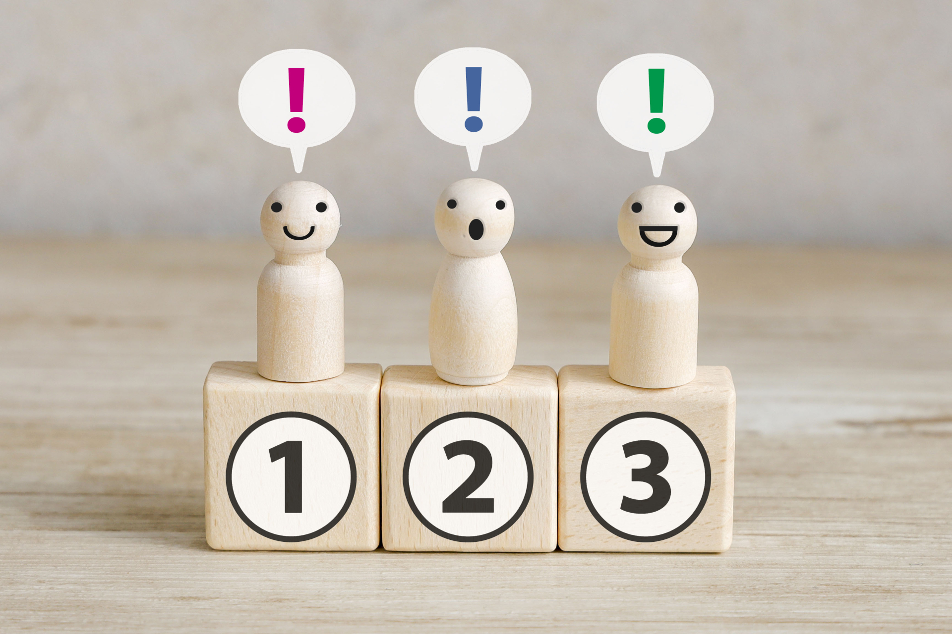 33173853_m | M Virtual(エムバーチャル) - Vライバーマネジメント事務所 Three wooden figures with speech bubbles showing colored exclamation marks (pink, blue, green) above numbered blocks 1, 2, 3, indicating different reactions.