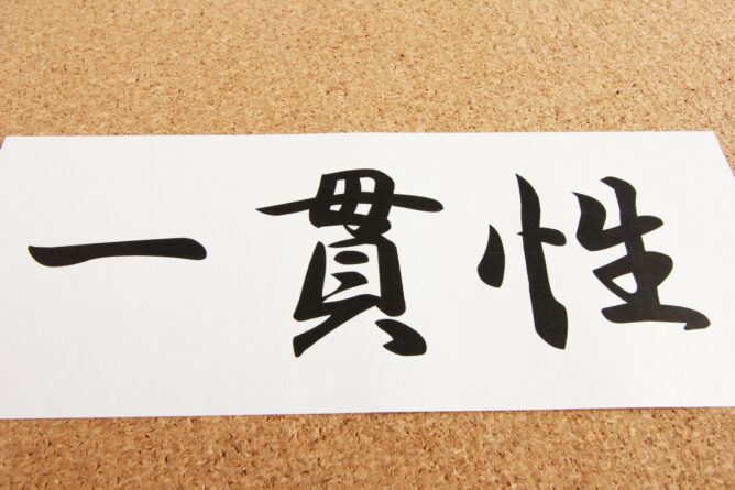 Close-up of bold black Japanese kanji characters printed on white paper resting on a corkboard.
