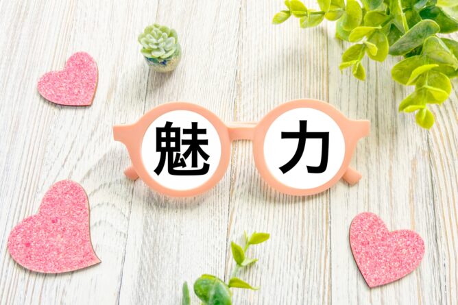 Pink novelty glasses with Chinese characters'魅力' on the lenses, surrounded by glittery pink hearts on a light wooden surface.