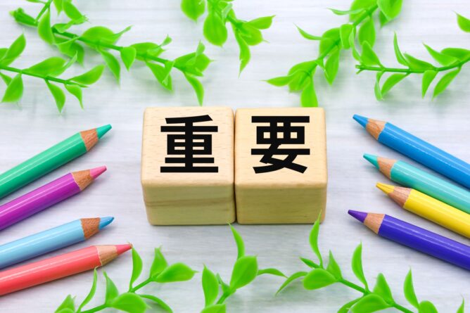 Two wooden blocks spell the Chinese word for 'important,' framed by colorful pencils and green leaves around them.