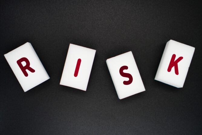 Four white tiles with red letters spell'RISK' on a dark background.