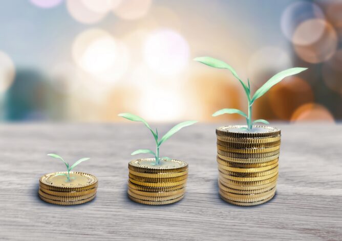 Three stacks of coins with young green plants growing from each, increasing in height from left to right, symbolizing investment growth.