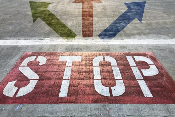 4248820_m | M Virtual(エムバーチャル) - Vライバーマネジメント事務所 Red STOP stencil on pavement with three arrows pointing in different directions (green, red, blue). This is a road-marking cue for drivers and pedestrians.