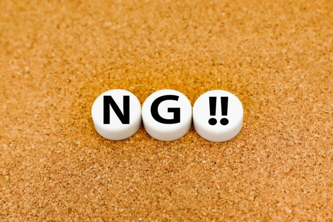 Three white circular tiles on a cork surface spell 'NG!!' in bold black letters.