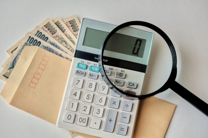 Calculator on a desk with a magnifying glass over Japanese yen banknotes and envelopes, suggesting financial review or accounting.