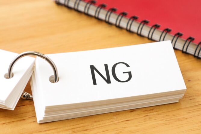 4490578_m | M Virtual(エムバーチャル) - Vライバーマネジメント事務所 A white name-tag card with the initials 'NG' resting in a ring binder on a wooden desk, with a spiral notebook in the background.