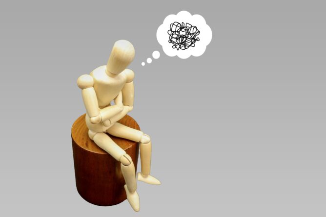 Wooden artist mannequin sitting on a stump, deep in thought with a scribbled thought bubble above its head.