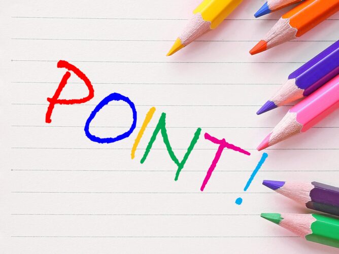 24368909_m | M Virtual(エムバーチャル) - Vライバーマネジメント事務所 Rainbow-colored letters spell 'POINT!' on a lined notebook, with colorful pencils arranged around the page.