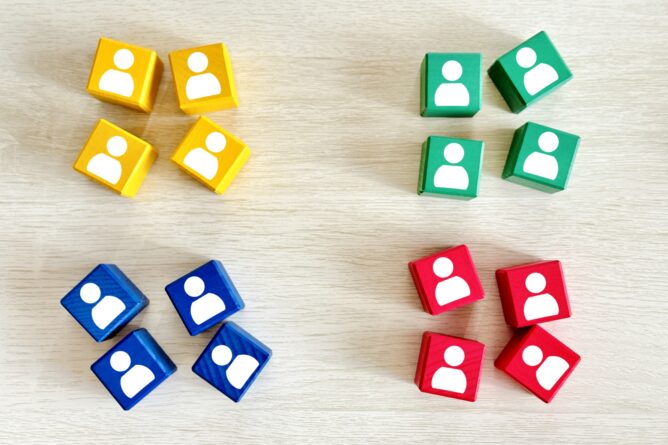 Four color groups of small cubes (yellow, green, blue, and red) each with a white user silhouette, arranged on a light wooden surface to imply separate teams or categories.