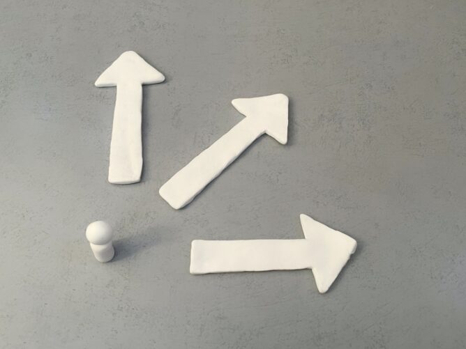 Three white clay arrows pointing up, right, and diagonally up-right on a gray surface, suggesting directions or choices.
