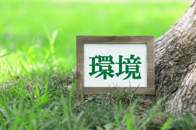 33198379_m | M Virtual(エムバーチャル) - Vライバーマネジメント事務所 Wooden-framed sign displaying the Chinese characters 環境 (environment) on grass next to a tree trunk outdoors.
