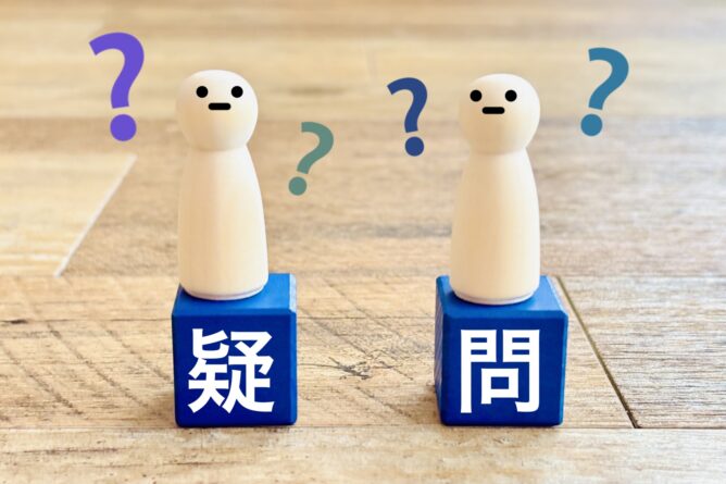 33916147_m | M Virtual(エムバーチャル) - Vライバーマネジメント事務所 Two small figures stand on blue blocks with Japanese characters for doubt (疑) and question (問), surrounded by colorful question marks to symbolize uncertainty and inquiry.