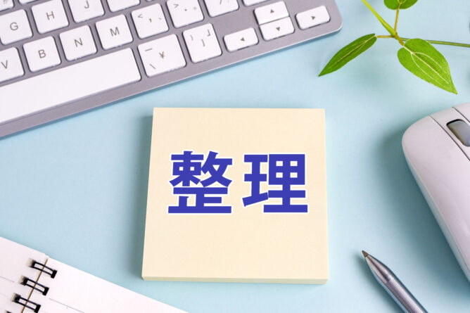 Sticky note with the Chinese characters for'organize' on a light blue desk, with a keyboard, mouse, plant, and notebook nearby, suggesting organizing tasks.