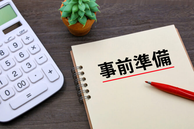 35059307_m 1 | M Virtual(エムバーチャル) - Vライバーマネジメント事務所 Notebook page shows the Japanese phrase 事前準備 with a red underline, on a desk with a calculator and a plant.