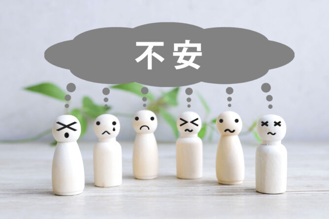 35342181_m | M Virtual(エムバーチャル) - Vライバーマネジメント事務所 Row of wooden figurines with distressed faces under a gray cloud labeled 不安, illustrating anxiety.