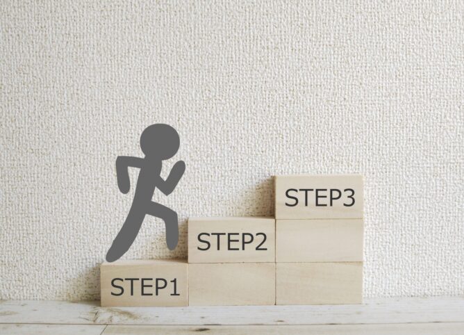 3919199_m | M Virtual(エムバーチャル) - Vライバーマネジメント事務所 Gray stick-figure runs up a three-step wooden staircase labeled STEP1, STEP2, STEP3 against a pale wall, illustrating progress.
