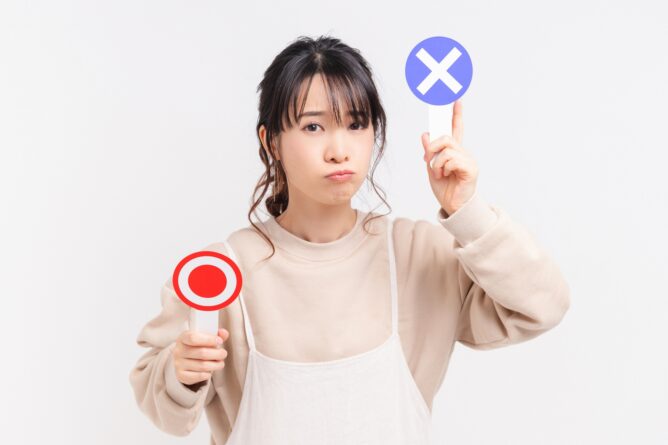 Woman with a puzzled expression, holding a red circular 'no/stop' sign in one hand and a purple X sign above her head, indicating disapproval or rejection.