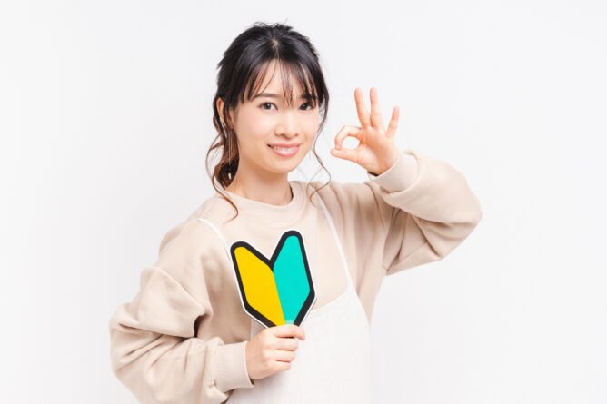 Smiling Asian woman holding a yellow-and-teal two-tone sign and giving an OK gesture with her right hand.